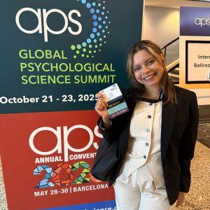 Photo of CUNY SPS Psychology student Beyra Thomas posing with ID at sign saying APS Global Psychological Science Summit. at APS Conference.