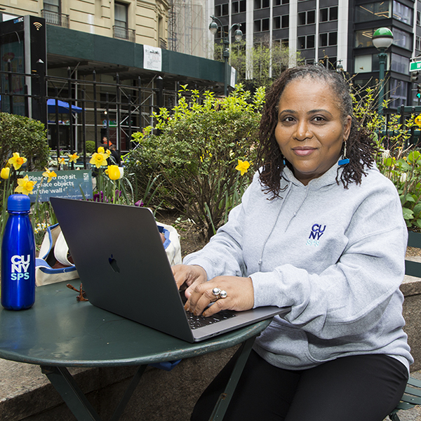 CUNY SPS student working on their laptop outside in a park