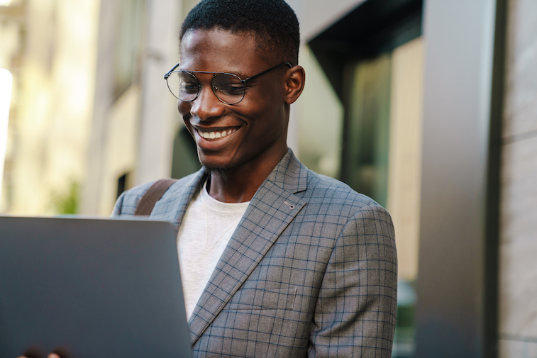 A joyful African American man smiling and using a laptop