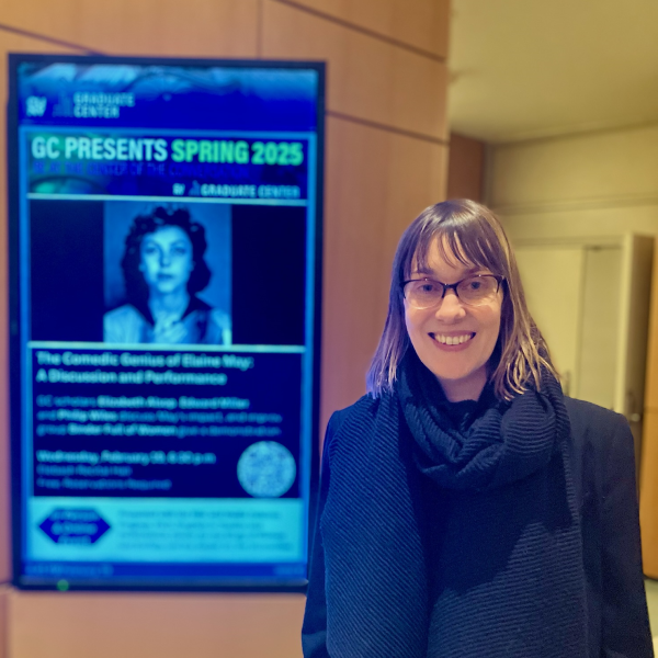 Photo of CUNY SPS Communication and Media Professor Elizabeth Alsop Standing In Front of Poster Announcing Her Talk at Graduate Center