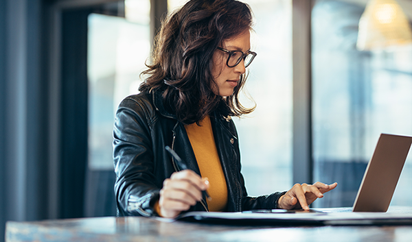 Woman on laptop with pen in hand